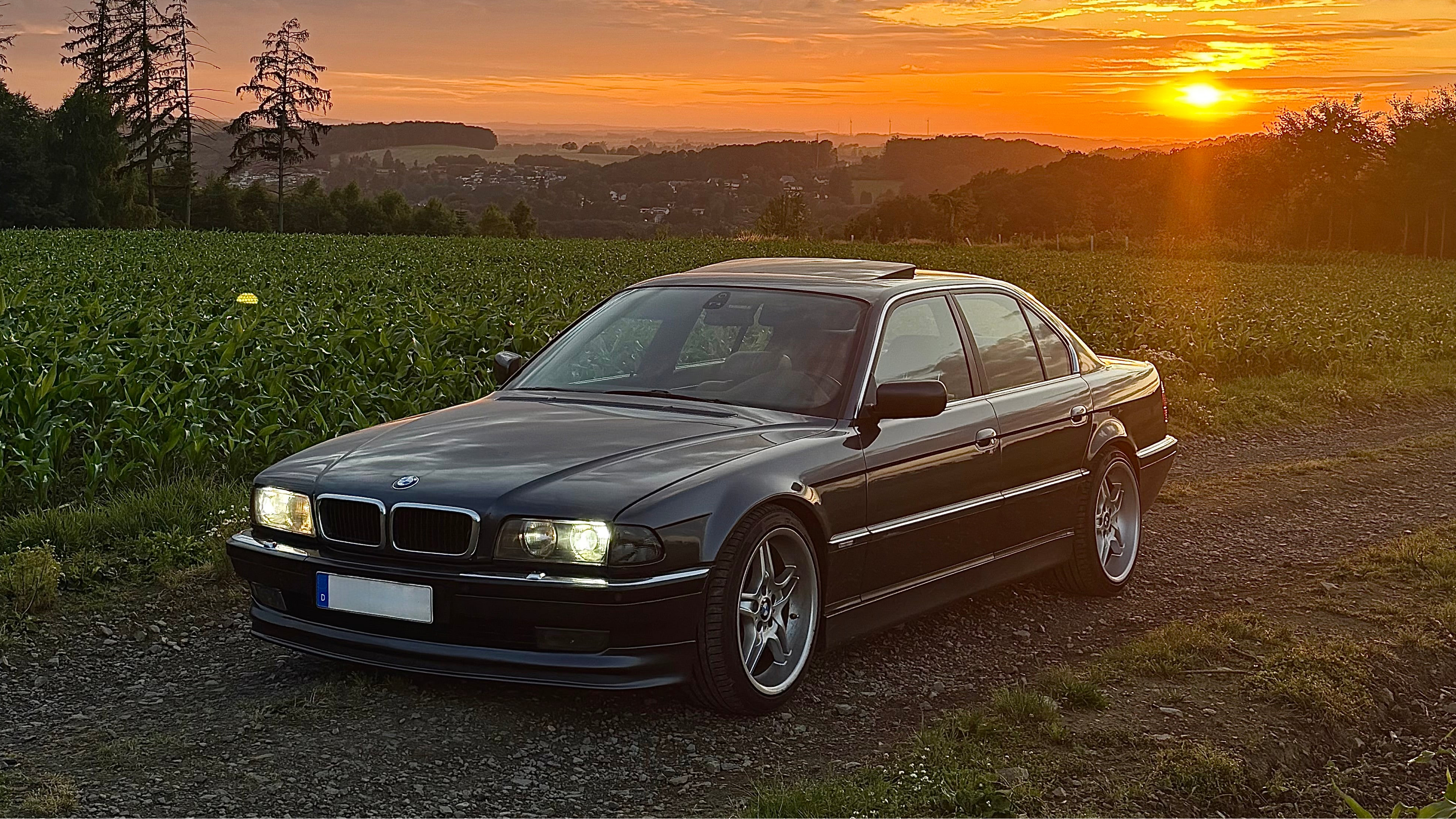 Ein tiefergelegter BMW E38 740i vor einem Sonnenuntergang.